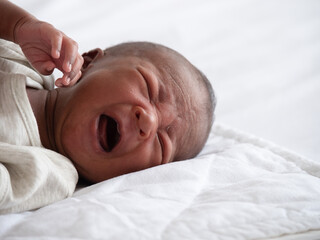 African American baby boy crying on a white bed.