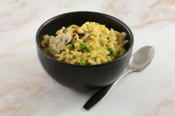 Orzo pasta with cheese and mushroom and peas side dish in black bowl with spoon