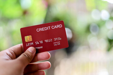 The person is holding a red credit card, a credit card can be used to pay for goods and services at retail stores, restaurants, or online shopping. Concept of using a credit card.