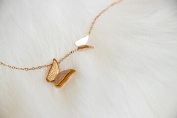 Closeup of a golden necklace with two butterflies pendant sitting on white fur as the background