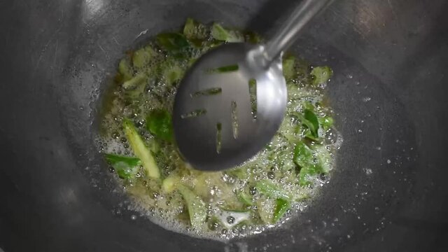 Slow motion Cooking food Stir-frying curry leaves in oil with green chilly and jeera , extreme close view.Sauteing in vessel with spoon