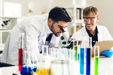 Professional two scientist man research and working doing a chemical experiment while making analyzing and mixing liquid in test tube.Young science man dropping sample chemical on glass at laboratory