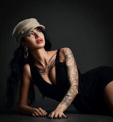 Sexy woman with pouty lips and tattoo in black evening dress with deep neckline is lying on floor...