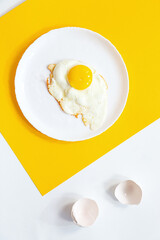 Fried egg on a white plate, on a yellow and white background. Minimal creative composition with copy space, top view.