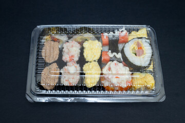 Big sushi set in transparent plastic box. Isolated on black background. Japanese food.