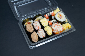 Big sushi set in transparent plastic box. Isolated on black background. Japanese food.