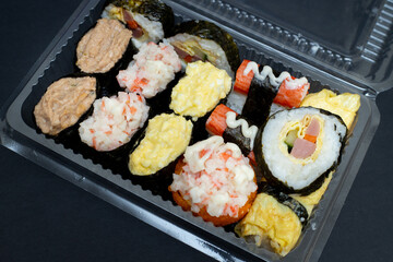Big sushi set in transparent plastic box. Isolated on black background. Japanese food.