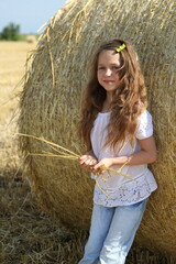 Naklejka na ściany i meble Little girl near a haystack in a field
