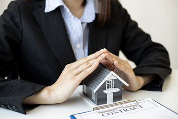 A female home salesperson puts both hands in a triangle pose on a gray miniature house model, Real estate trading ideas.