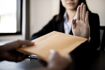 Obraz premium Businesswoman raised her hand to deny accepting a bribe from a business partner, a brown envelope containing a large number of dollar bills as money for bribery, a corruption concept.