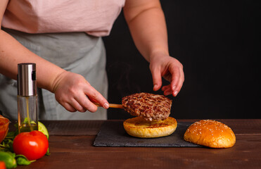 A close-up of a delicious burger being prepared. The cook puts a juicy fried cutlet on top of a toasted bun. Gastronomy, recipes, menus, fast food. Juicy burger