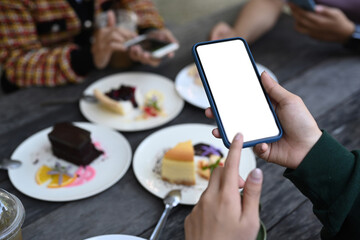 Close up view of young female using mobile phone taking photo of sweet dessert  during spending time with her friends at cafe.