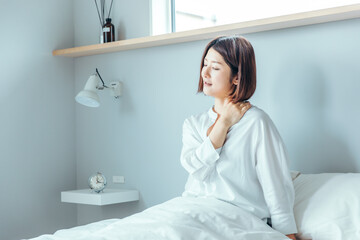 30代女性が綺麗なベットの上で朝起きて肩が痛く抑えている