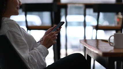 Happy young woman using mobile phone while relaxing at coffee shop.