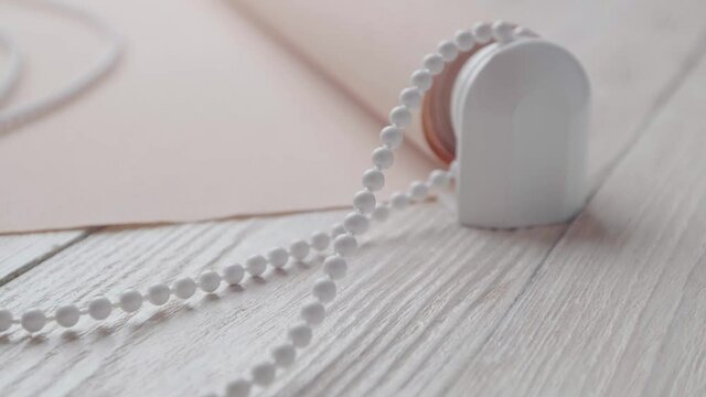 Beige roller blind and spare parts on a white wooden table. Preparation for the installation of roller blind.