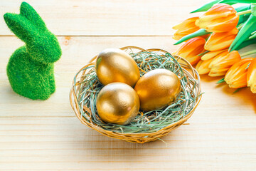 Golden easter colour eggs in basket with spring tulips, white feathers on wooden background in Happy Easter decoration. Spring holiday concept.