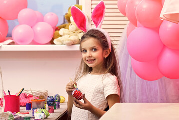 Baby girl paint handmade egg at party balloons. Child with happy face hold easter eggs.