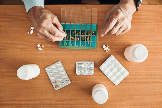 Senior man organizing his medication into pill dispenser. Senior man taking pills from box. Healthcare and old age concept with medicines. Medicaments on table