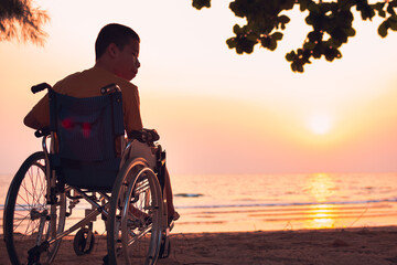 Asian special child on wheelchair on the sea beach with sunset on travel time in holiday family and learning about nature around the sea,Lifestyle in the education age kids,Happy disabled kid concept.