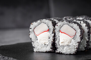 appetizing sushi roll with Philadelphia cheese and crab stick in black sesame on a black stone plate