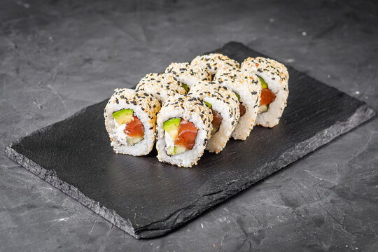 appetizing california sushi roll with cheese avocado cucumber and salmon in sesame seeds on a black stone plate