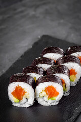 appetizing sushi roll futomaki with cucumber and salmon on a black stone plate