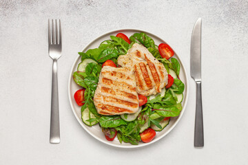 Fresh salad - cucumbers, tomato, arugula, chards leaves and chicken fillet grill in a plate on the table. Top view. Healthy diet food.