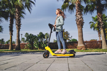 Young casual modern active millennial woman using electric scooter for fast mobile riding through...