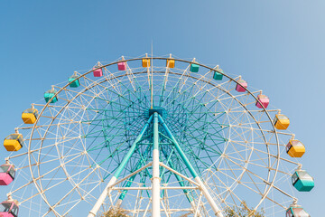 Colorful ferris wheel in an amusement park against blue sky