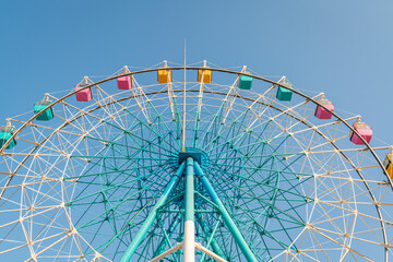 Colorful ferris wheel in an amusement park against blue sky