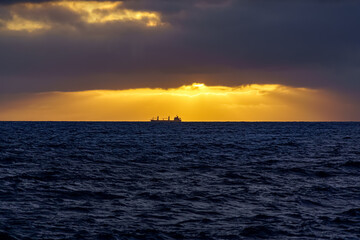 Obraz premium Freighter ship in the distance above the sea horizon on a sunset with dramatic sky. Gran Canaria. Spain