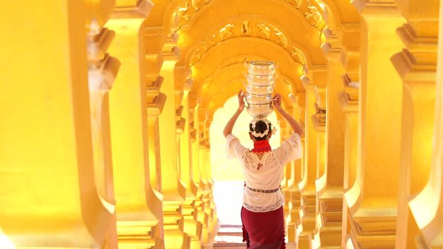 Young woman with traditional burmese holding bowl of rice on the head at beautiful golden pagoda in Myanmar.