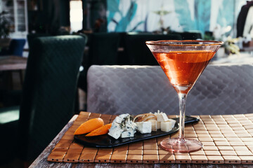 Red orange alcoholic cocktail with cheese plate in cafe.