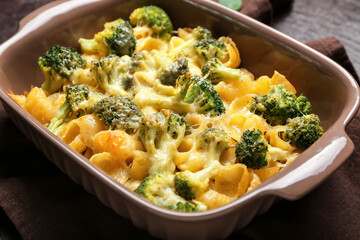 Tasty baked pasta with broccoli and cheese in baking dish on dark background, closeup