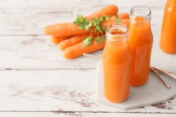 Bottles of healthy carrot juice with ingredients on light wooden background