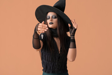 Evil young witch with pendulum on color background
