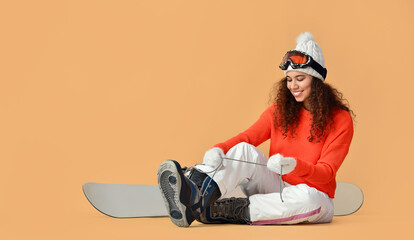 Female snowboarder putting on shoes against color background