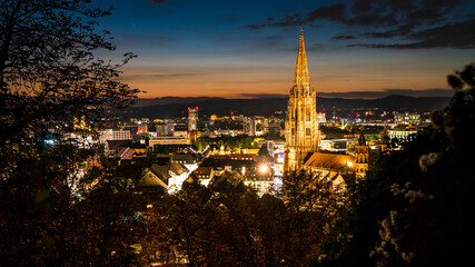 Naklejka premium Germany, Freiburg im Breisgau, Magical orange sunset sky above skyline of the beautiful city and muenster by night in blue hour atmosphere