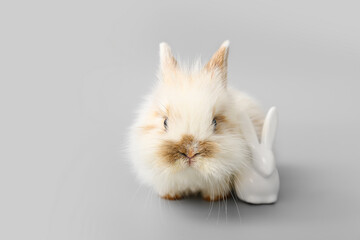 Cute fluffy rabbit and decorative figurine on grey background