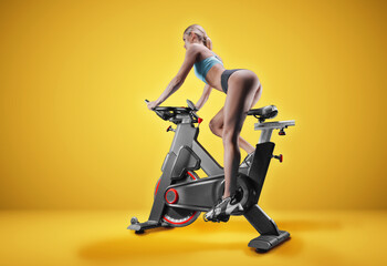 Long-legged girl posing in the studio on an exercise bike. Orange background. The concept of...