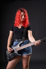 Teenager girl with red hair plays the electric guitar on a black background