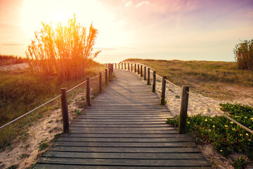 Wooden walkway on the sandy seashore in the magical light of the sunset. Beautiful seascape in the evening