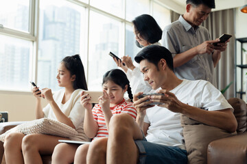 Fototapeta premium Fear of missing out, FOMO people. Social media addiction concept, Everyone in family using mobile phone in the living room. Problem of family relationships from mobile phone addiction.