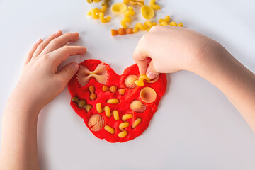 Fine motor skills. Kids creativity. Plasticine modeling for child development at home. Childs hands creating heart from dough for modeling. Anti-stress game with pasta