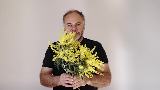 Handsom mature bearded man smiling and giving mimosa flower to viewer. Man with bouquet.Holiday concept. Slow motion.