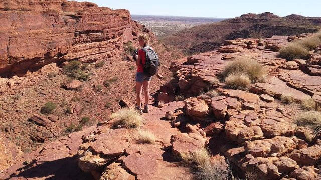Photographer woman taking pictures at Kings Canyon in Watarrka National Park, Australia's Red Center. Tourist relaxes during the Rim Walk to edge of canyon. Northern Territory, Outback Australia.