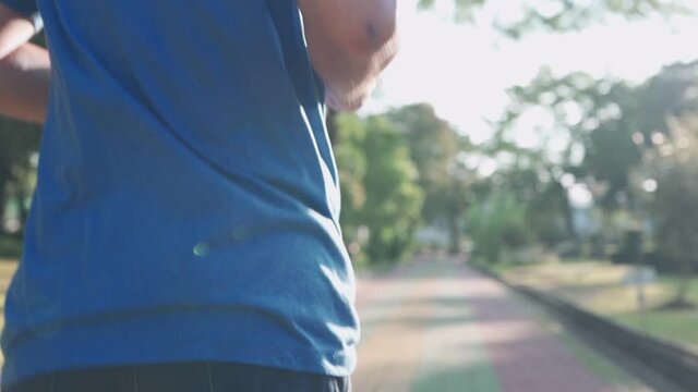Rear view of senior male running on the running track at the exercise park on a sunny day in slow motion. mid body section, active lifestyle, illness prevention motivation come back after pandemic