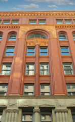 An upward, frontal view of an office building with rusticated sandstone base and stone carvings, an eight-story building with a strong example of Romanesque Revival architecture - vertical format