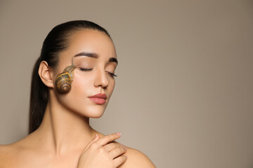 Beautiful young woman with snail on her face against beige background. Space for text