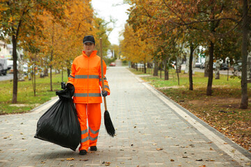 Street cleaner with broom and garbage bag outdoors on autumn day